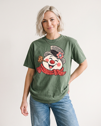 Blonde woman wearing a Moss green vintage snowman Christmas graphic T-shirt with blue jeans.