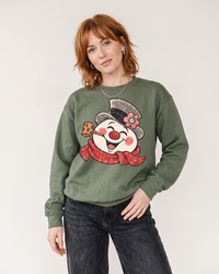 Red-haired woman wearing a Military Green vintage snowman Christmas sweatshirt with dark jeans.