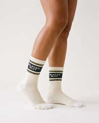 Ivory Pilates Slut crew grip socks with charcoal lettering and yellow stripes modeled on woman's legs