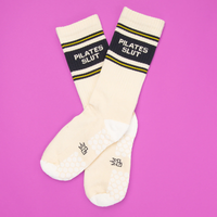 Pair of ivory Pilates Slut grip socks with black lettering and yellow athletic stripes