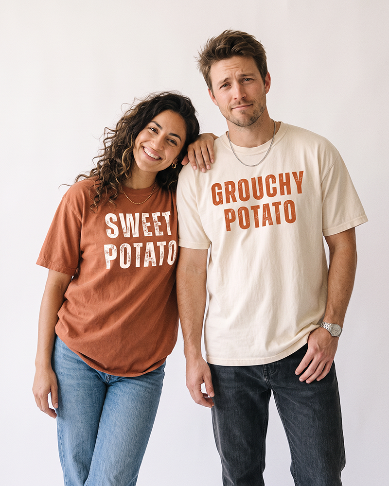 Couple wearing matching Sweet Potato and Grouchy Potato heavyweight graphic tees in Yam orange and Ivory.