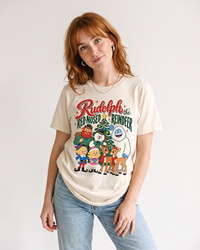 Woman with auburn hair wearing a Natural Rudolph vintage Christmas graphic tee with blue jeans, featuring Rudolph and friends gathered around a Christmas tree.