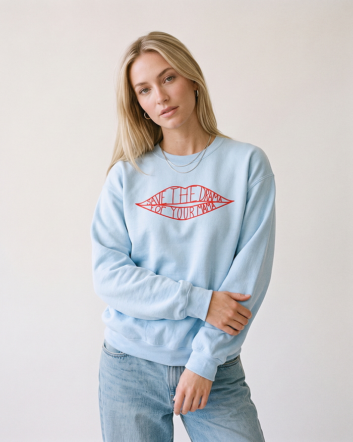 Blonde woman wearing a light blue Save The Drama For Your Mama sweatshirt with light wash jeans.