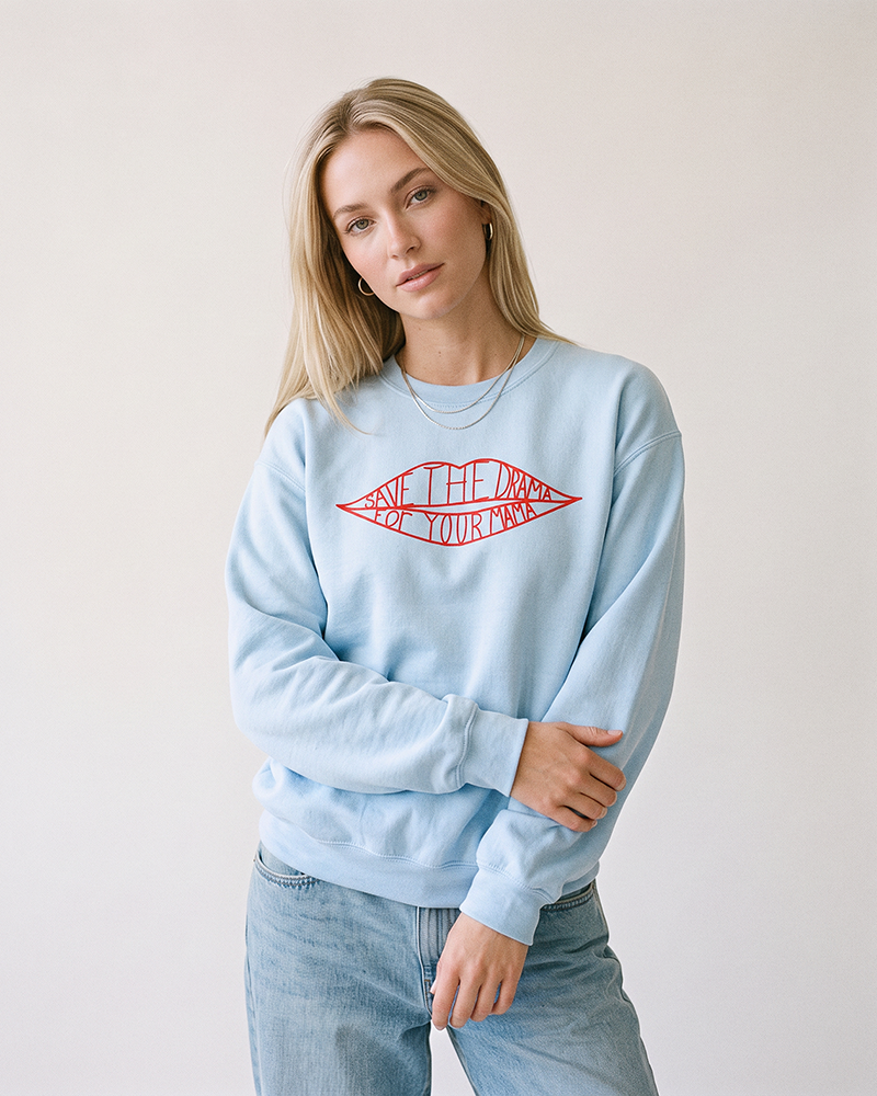 Blonde woman wearing a light blue Save The Drama For Your Mama sweatshirt with light wash jeans.