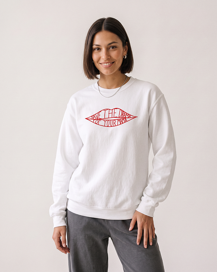 Brunette woman wearing a white Save The Drama For Your Mama graphic crewneck sweatshirt with gray pants.