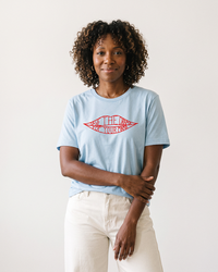 Woman with curly hair wearing light blue Save The Drama For Your Mama graphic tee and cream pants.
