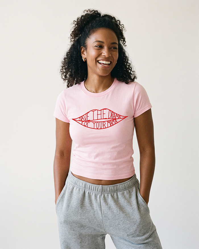 Woman wearing a fitted light pink graphic baby tee with red lips design and grey sweatpants.
