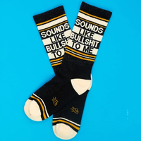 Pair of black Sounds Like Bullshit To Me socks with cream text panels and mustard-gold stripes