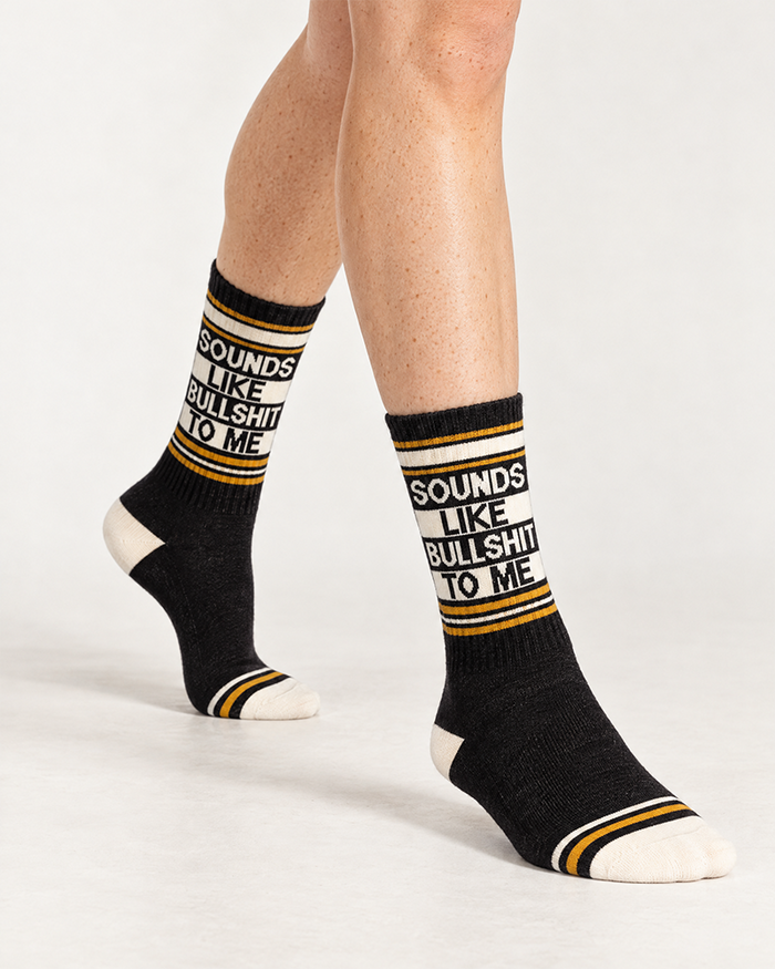 Model wearing black Sounds Like Bullshit To Me gym socks with cream lettering and gold stripes