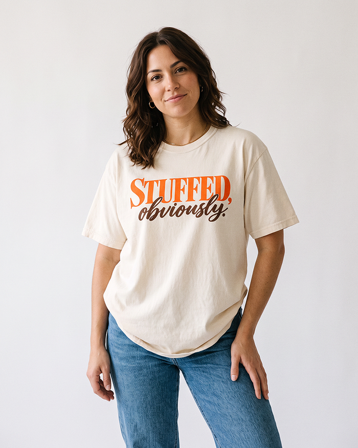 Woman wearing an ivory Stuffed, Obviously heavyweight Thanksgiving graphic tee with blue denim jeans.