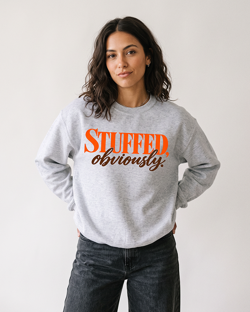 Brunette woman modeling an ash gray Stuffed, Obviously Thanksgiving graphic sweatshirt with vintage black denim jeans.