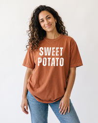 Woman wearing a Yam orange Sweet Potato heavyweight graphic tee with white distressed lettering and light wash jeans.