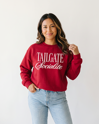 Woman wearing cardinal red Tailgate Socialite crewneck sweatshirt with white graphic and light wash jeans