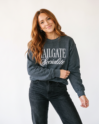 Woman wearing dark heather Tailgate Socialite crewneck sweatshirt with white graphic and black jeans