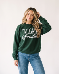 Woman wearing forest green Tailgate Socialite crewneck sweatshirt with white graphic and jeans
