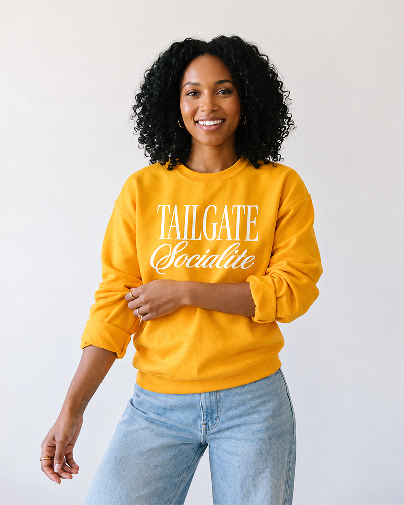 Woman wearing gold Tailgate Socialite crewneck sweatshirt with white graphic, women's game day sweatshirt