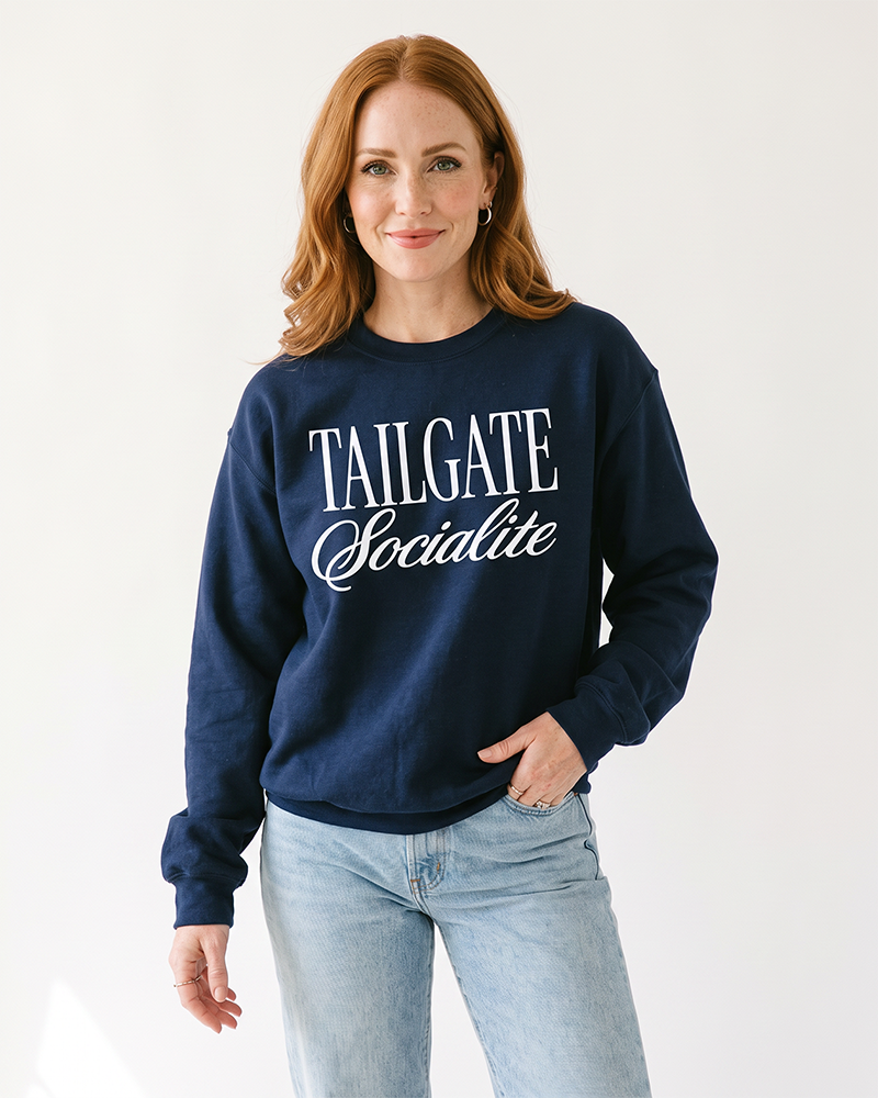 Red-haired woman wearing navy Tailgate Socialite crewneck sweatshirt with white graphic and jeans