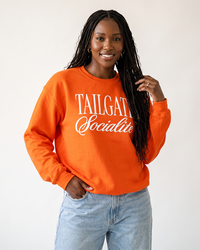 Woman wearing orange Tailgate Socialite crewneck sweatshirt with white graphic, football tailgate outfit
