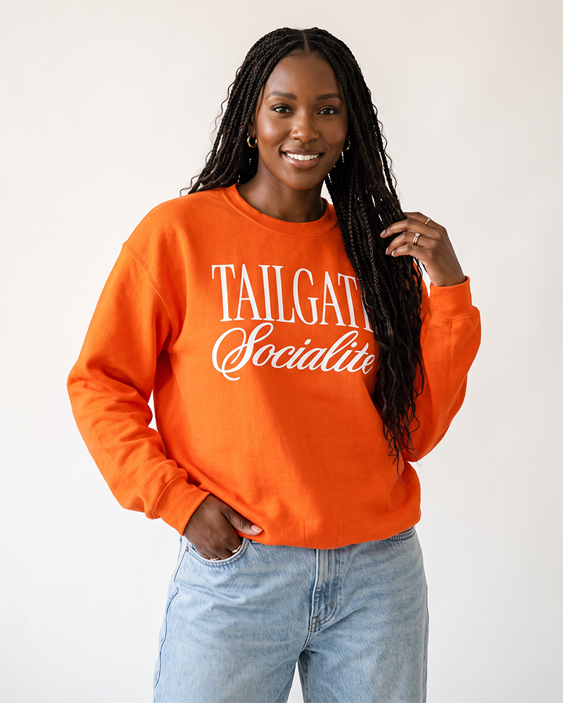 Woman wearing orange Tailgate Socialite crewneck sweatshirt with white graphic, football tailgate outfit