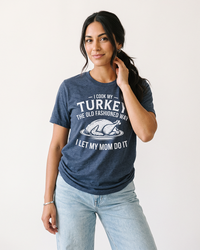 Woman wearing a Heather Navy I Cook My Turkey funny Thanksgiving graphic T-shirt with light wash jeans and a relaxed casual fit.