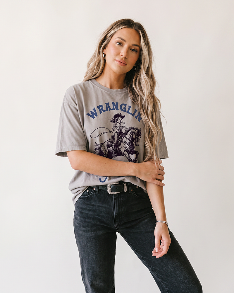 Woman wearing grey Wranglin My Feral Kids cowgirl mom heavyweight graphic tee